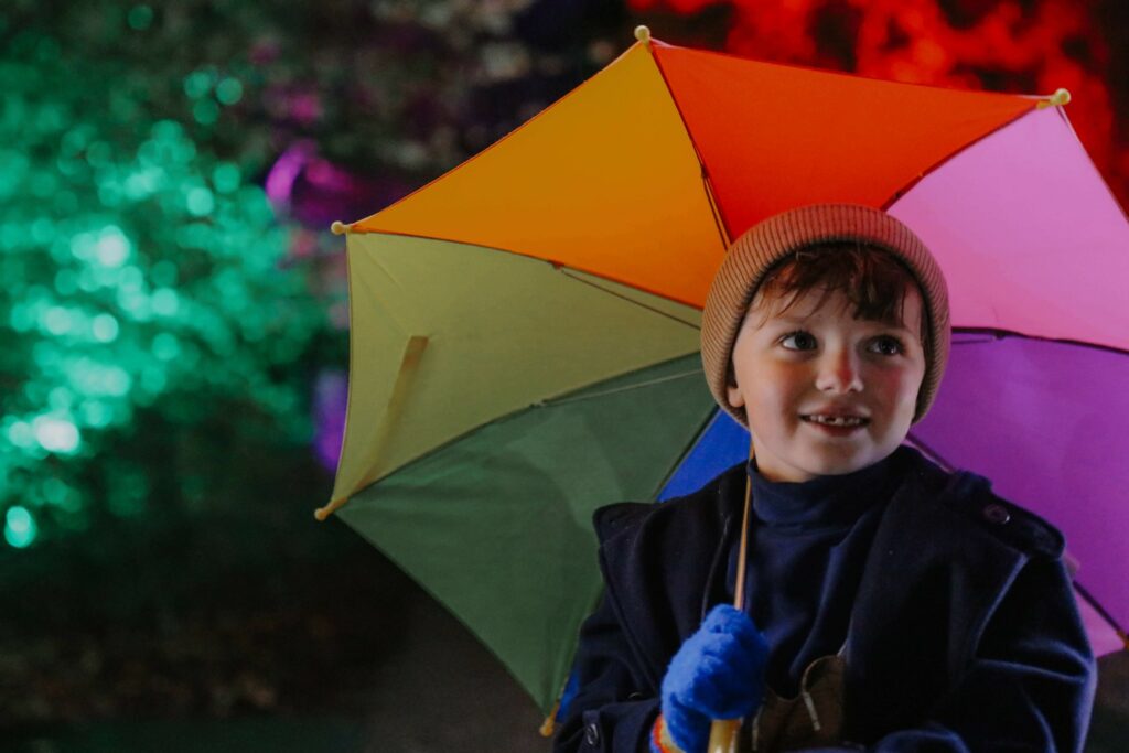 A little boy under a rainbow umbrella at glow Marwell, Marwell Zoo