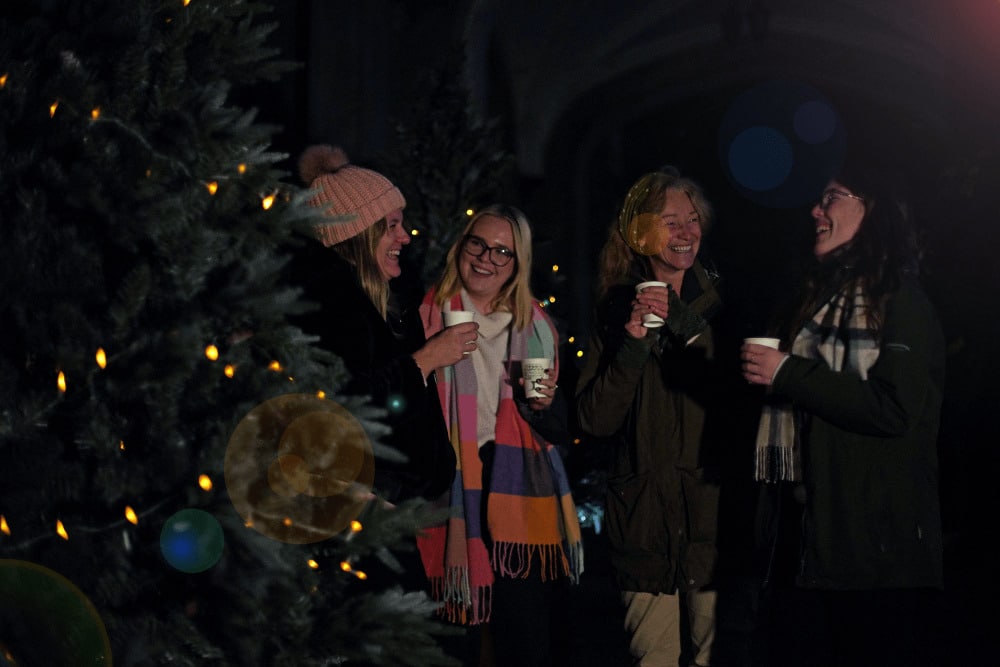 A group of colleagues laugh together while surrounded by sparkling Christmas trees