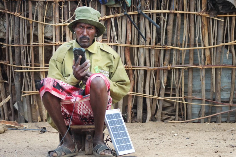 A Marwell Wildlife Community Scout in Kenya sits with a portable solar panel