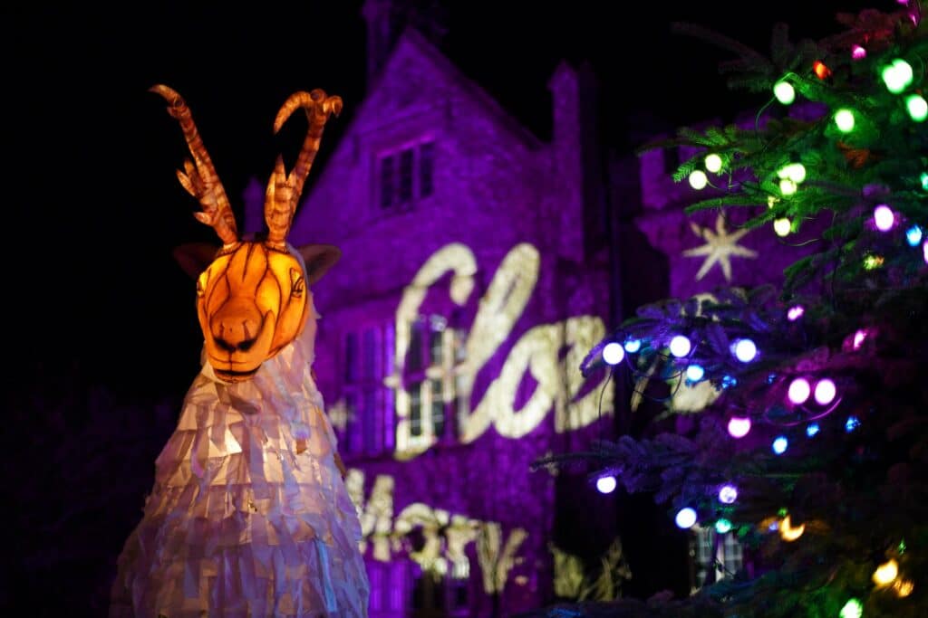 A Ghost caribou lantern costume stands in front of a lit-up Marwell Hall at Marwell Zoo's Glow Marwell event