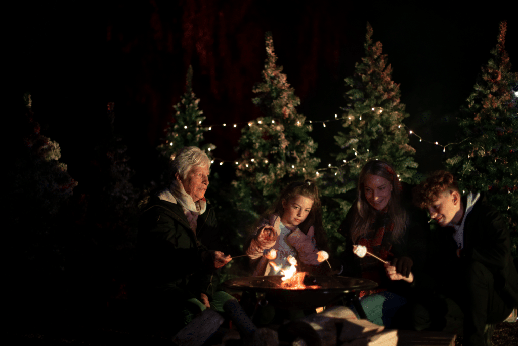 A family sit around a fire to roast marshmallows at Glow Marwell