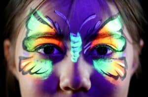 UV butterfly facepaint brightly glows around a young girl's eyes.