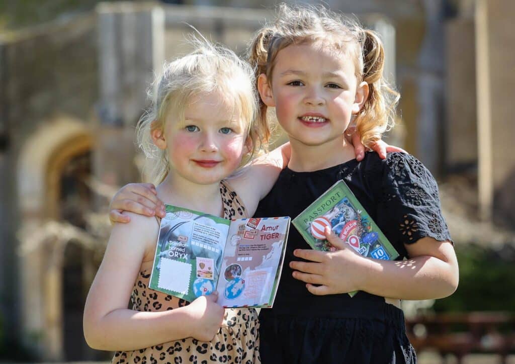 Two girls holding the Marwell Explorer Passport booklet outside Marwell Hall