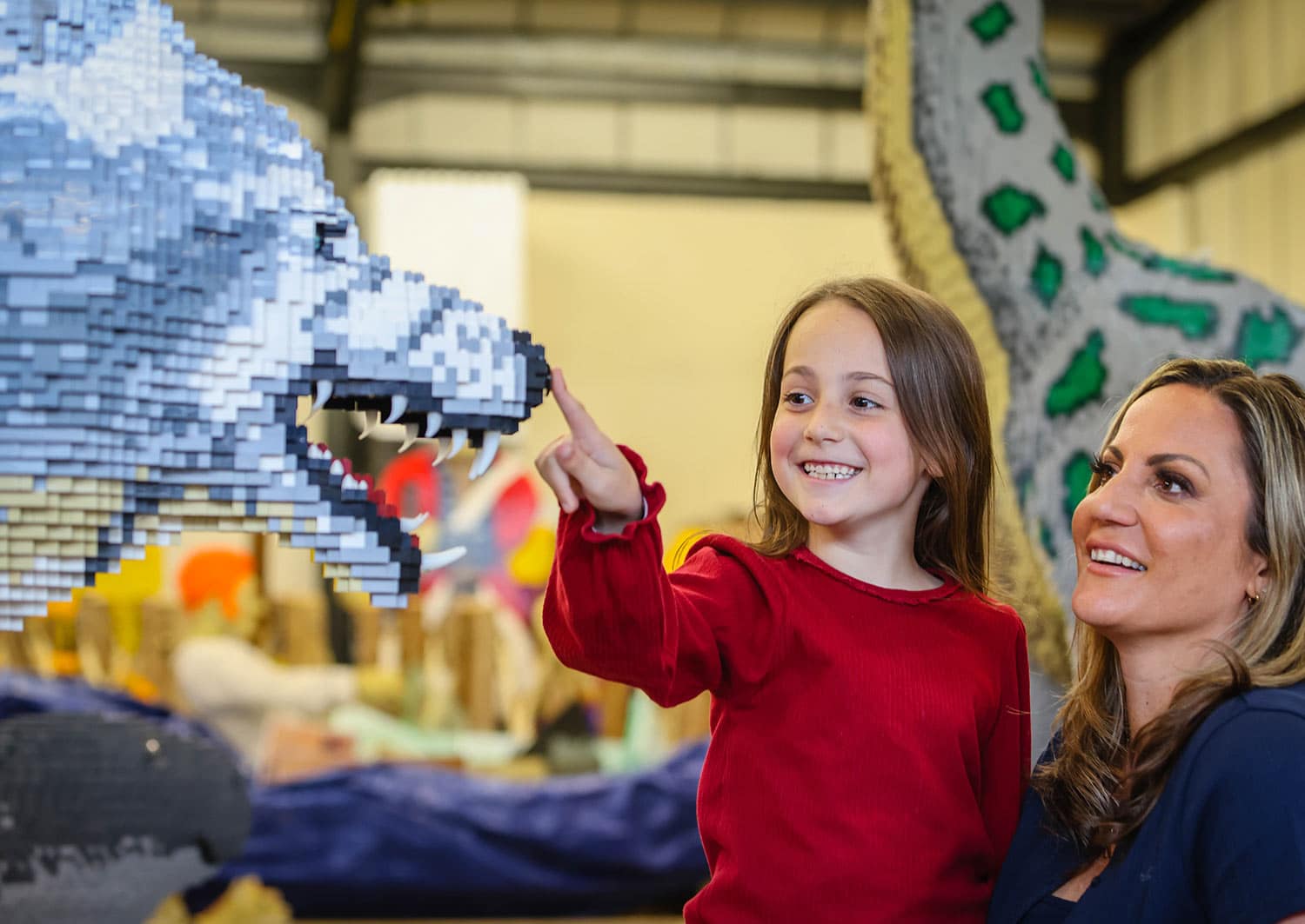 A girl presses the button on the nose of a Dire Wolf made of toy bricks to make it growl
