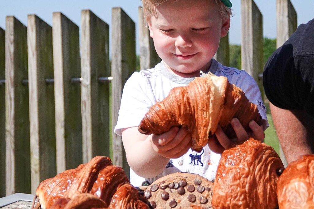 A boy smiles as he looks at a croissant and pastries at Marwell Zoo