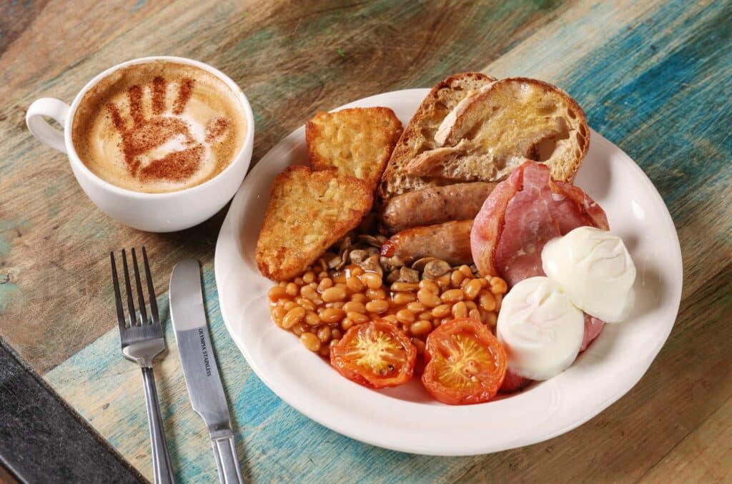 The Keeper's Breakfast at The Keeper's Kitchen. With hash browns, tomatoes, baked beans, bacon, sausages, eggs and toast. Plus a hot drink with a Marwell handprint logo dusting.