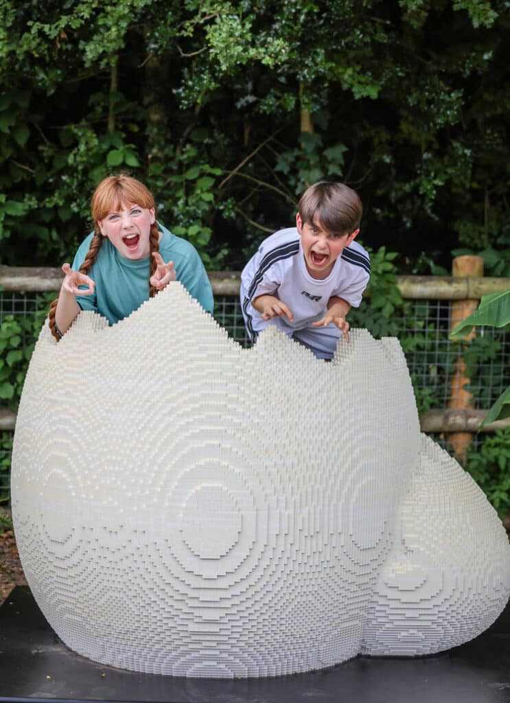 Two people pose as dinosaurs in a dinosaur egg made of toy bricks at Marwell Zoo's Extinction event