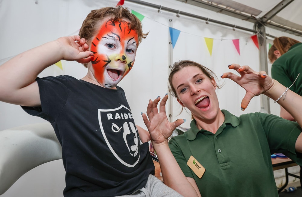 A little boy with his face painted as a tiger poses with a Marwell Zoo team member at the Extinction brick event