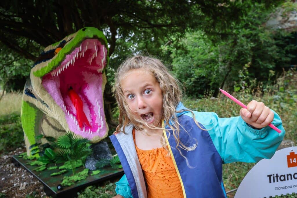 A girl pretends to scream and run away from a titanoboa made of toy bricks at Marwell Zoo's Extinction event