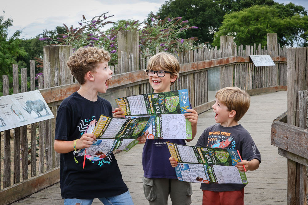 Three boys at Marwell Zoo holding paper trails of the Extinction event map
