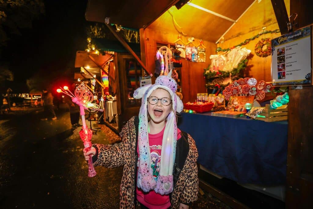 A child holding a butterfly glow stick by a stall at the Glow Marwell festive market