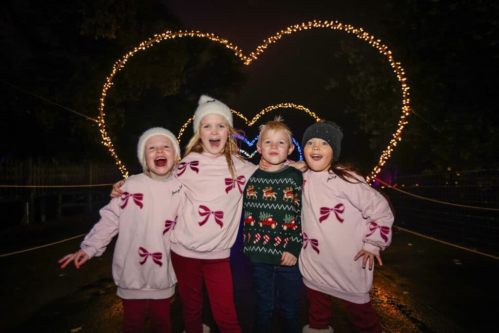 Four children smile by the heart arch at Glow Marwell light trail at Marwell Zoo