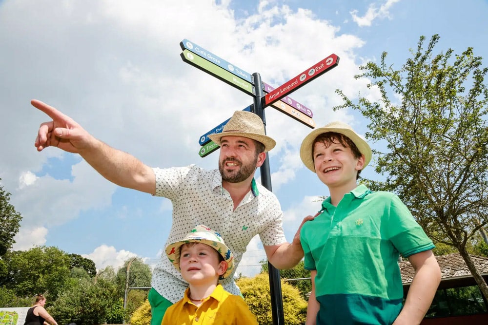 Guests at Marwell zoo stand under a sign and point in direction of