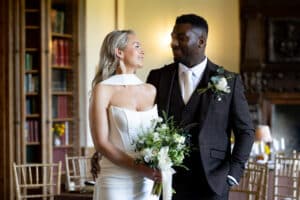 A wedding couple smile at each other in the Seymour Library, a wedding venue at Marwell Hall
