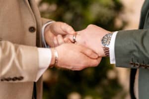 Close up shot of a groom putting a ring on the hand of another groom at a wedding at Marwell Zoo