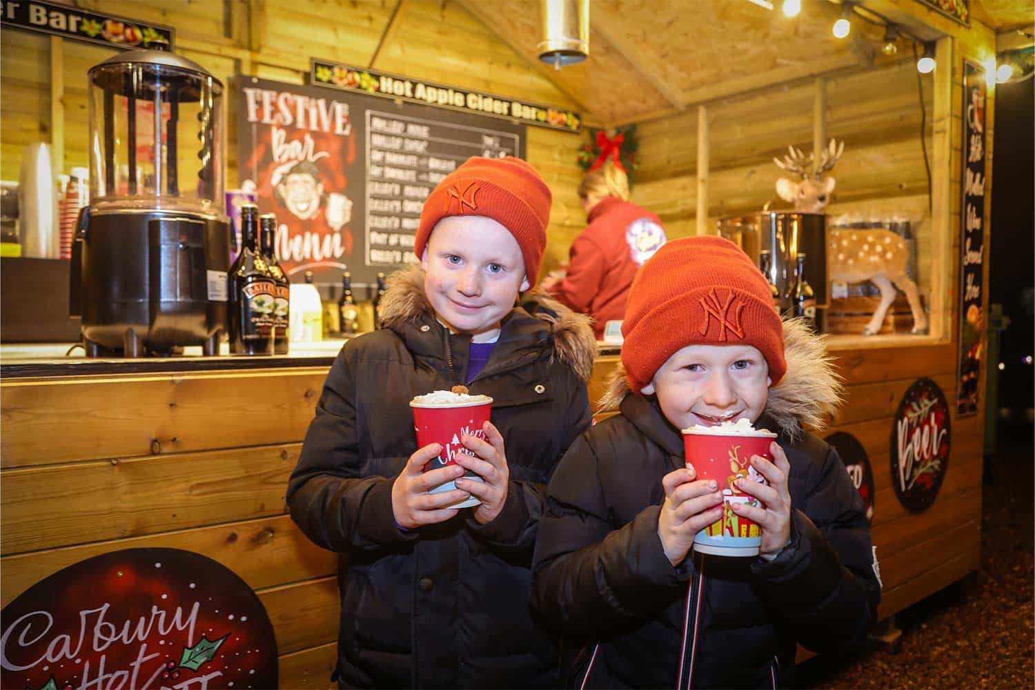 Two children drink hot chocolate outside a festive market stall at Marwell Zoo